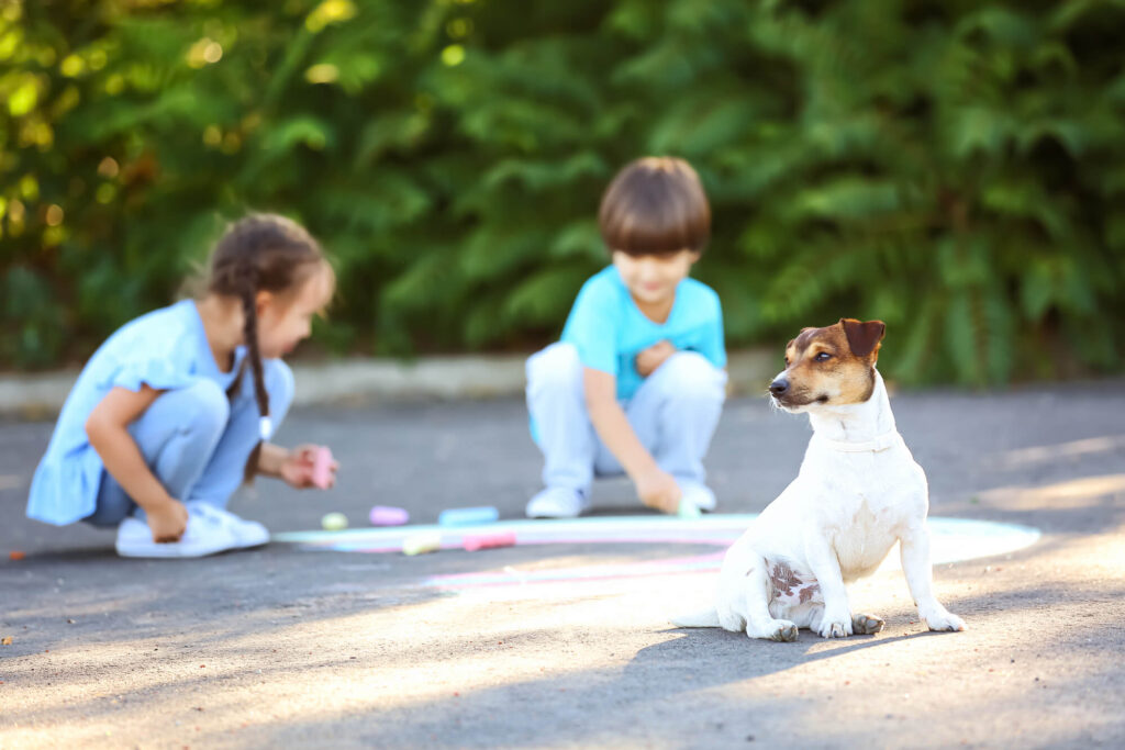 dog sitting on floor next to children playing with chalk